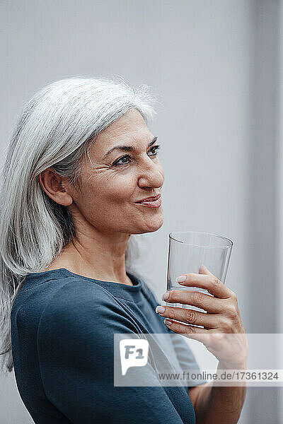 Geschäftsfrau schaut weg  während sie an der Wand im Büro Wasser trinkt