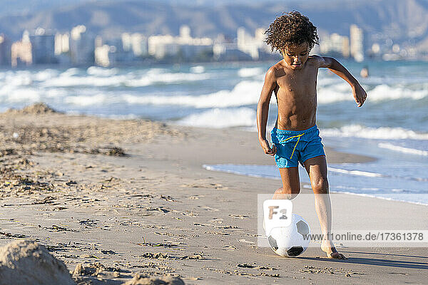 Shirtless boy playing with soccer ball at beach