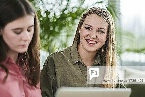 Happy blond female trainee sitting by businesswoman in office