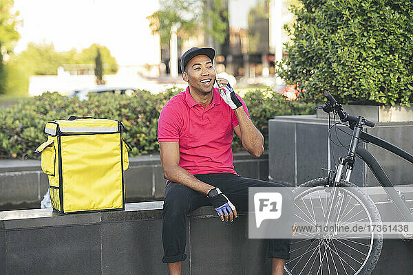 Happy delivery man looking away while talking on smart phone
