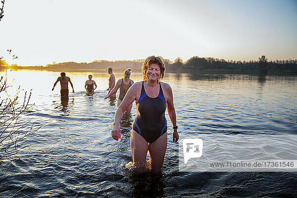 Lächelnde reife Frau im Wasser stehend mit männlichen und weiblichen Freunden im Hintergrund