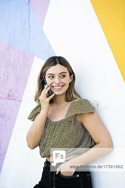 Lächelnde Frau  die wegschaut  während sie mit einem Mobiltelefon spricht