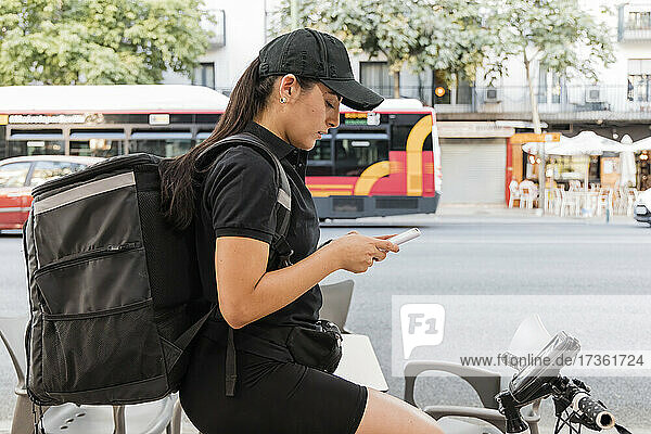 Young female delivery person using smart phone on bicycle