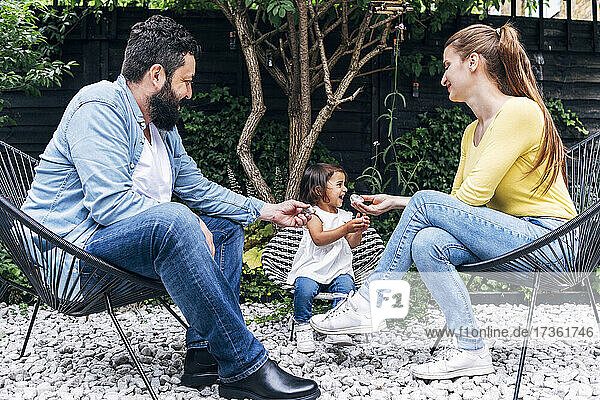 Smiling parents holding pebble while sitting by daughter at back yard