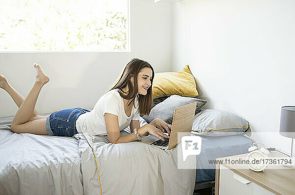 Young woman using laptop while lying on bed in bedroom at home
