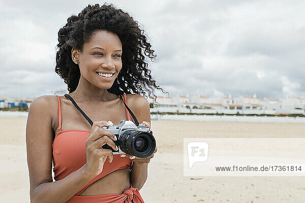 Lächelnde schöne junge Frau mit Vintage-Kamera am Strand