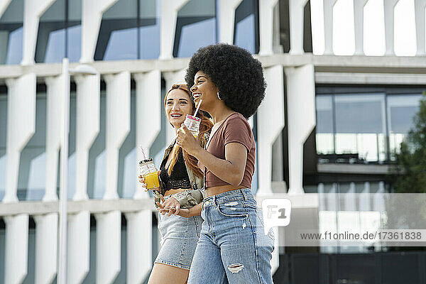 Glückliche multiethnische Freundinnen halten sich beim Spaziergang in der Stadt an den Händen