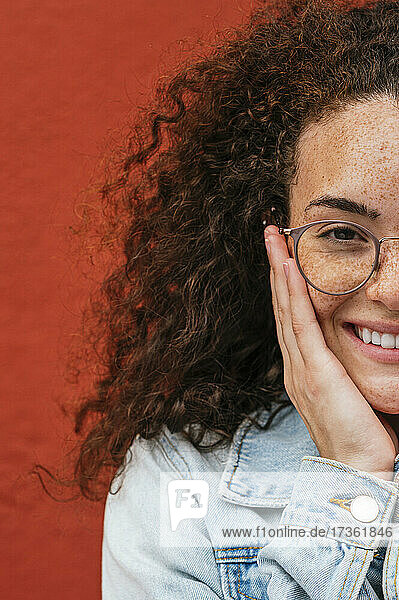 Lächelnde junge Frau mit Brille vor einer roten Wand