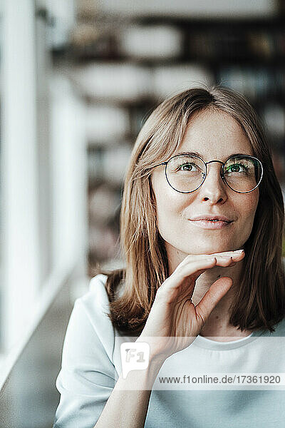 Young woman wearing eyeglasses sitting with hand on chin in cafe