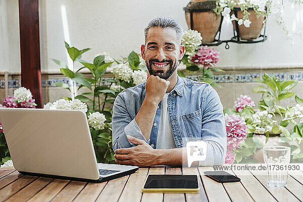 Bearded businessman with hand on chin sitting at desk in backyard