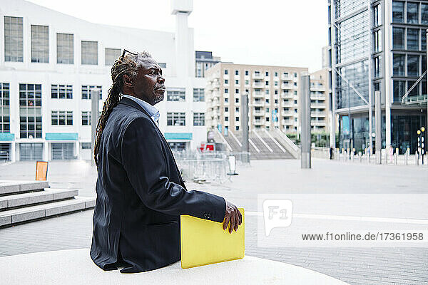 Älterer Geschäftsmann hält gelben Laptop in der Hand  während er in der Stadt sitzt