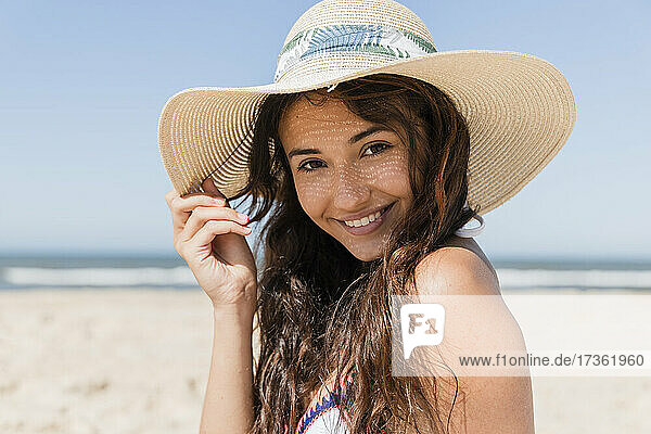 Lächelnde Frau mit Sonnenhut am Strand im Urlaub