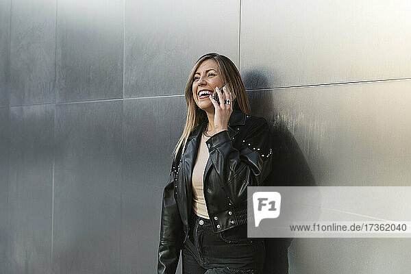 Glückliche Frau  die mit ihrem Handy telefoniert  während sie vor einer Metallwand steht