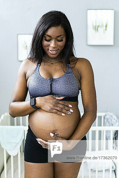 Smiling pregnant woman touching abdomen in bedroom
