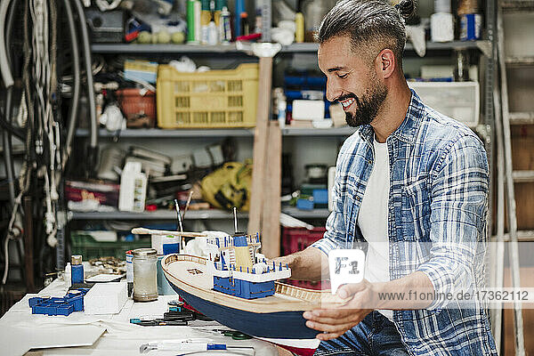 Lächelnder Handwerker bei der Arbeit an einem Schiffsmodell in der Werkstatt