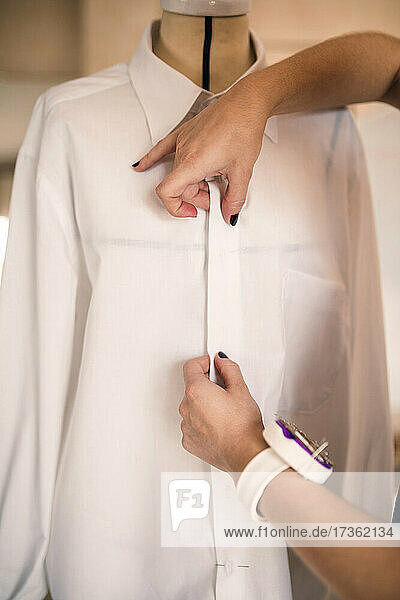 Weibliche Modedesignerin mit Nadelkissen-Armband  die ein Hemd an einer Schaufensterpuppe anpasst