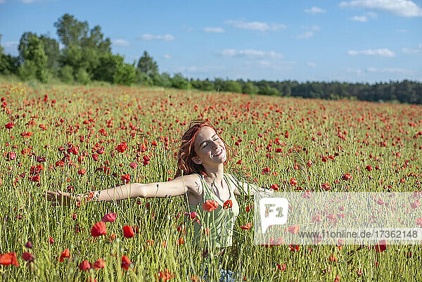Redhead girl with arms outstretched enjoying at poppy field on sunny day