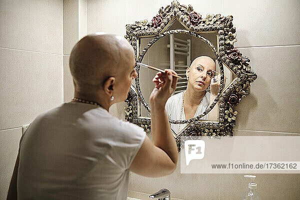 Mature woman with cancer brushing eyebrow while looking at reflection in mirror