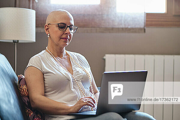 Glatzköpfige Frau benutzt Laptop im Wohnzimmer zu Hause