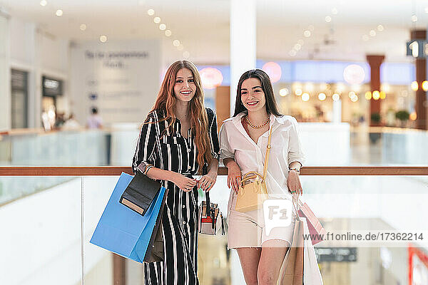 Smiling woman with shopping bags standing by female friend in mall
