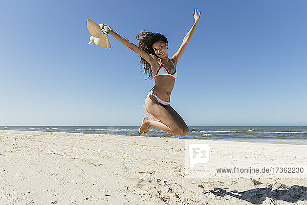 Carefree woman with arms raised jumping at beach