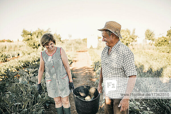 Lächelndes älteres Paar mit Gemüsekorb auf dem Bauernhof