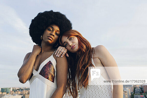 Young redhead woman leaning on Afro girlfriend's shoulder during sunset