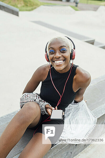 Lächelnde junge Frau mit Mobiltelefon hört Musik über Kopfhörer auf dem Sitz
