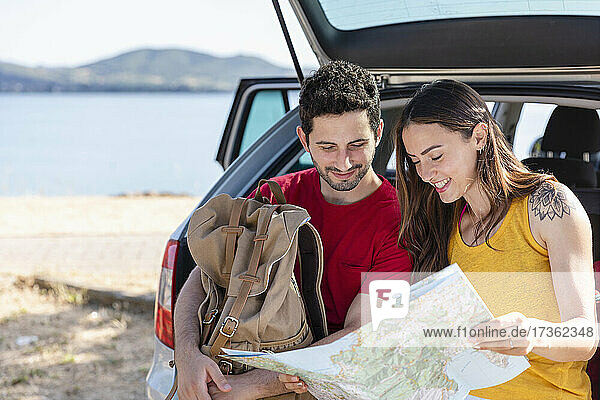 Boyfriend holding backpack while checking map with girlfriend during road trip