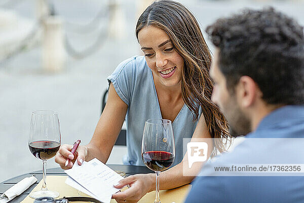 Lächelnde Frau zeigt ihrem Freund im Restaurant eine Postkarte