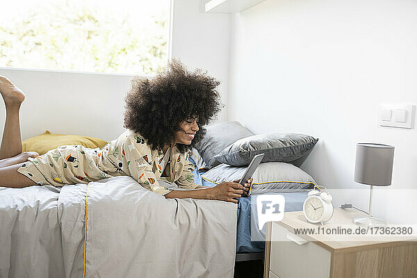 Frau benutzt digitales Tablet  während sie zu Hause im Bett liegt