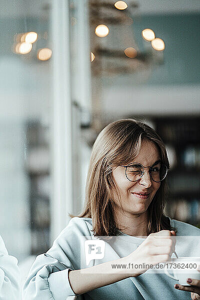 Junge Frau mit Kaffeetasse und zwinkerndem Auge in einem Café sitzend