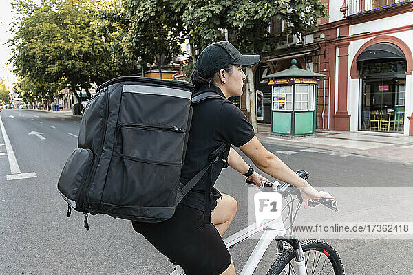Weibliche Lieferperson mit Rucksack auf dem Fahrrad auf der Straße