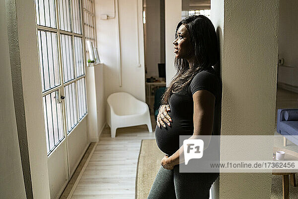 Nachdenkliche junge schwangere Frau  die sich zu Hause an eine Säule lehnt