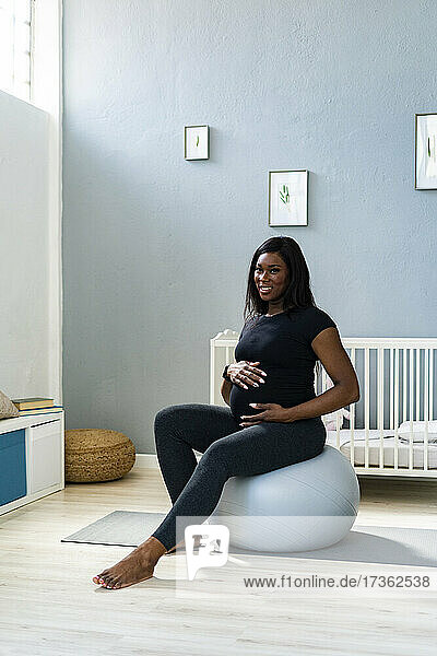 Glückliche schwangere junge Frau  die zu Hause auf einem Fitnessball sitzt
