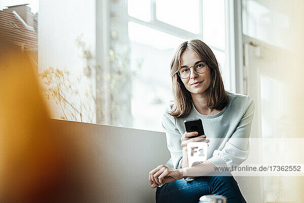 Junge Frau sitzt mit Mobiltelefon in einem Café