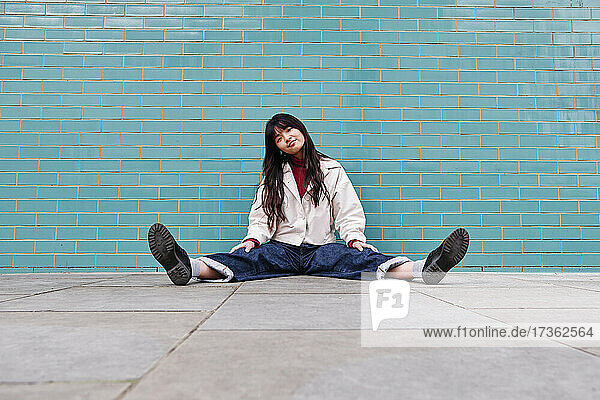 Schöne junge Frau sitzt mit gespreizten Beinen vor einer Backsteinmauer