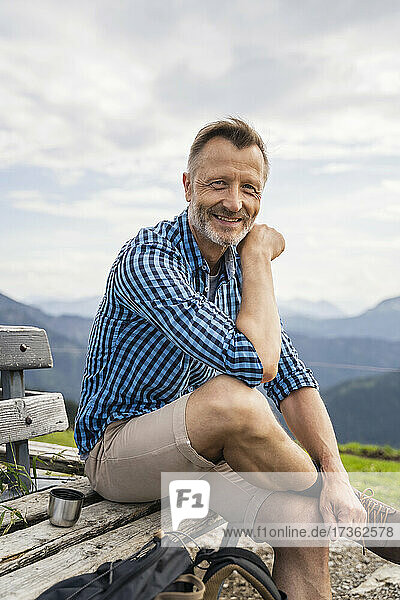 Lächelnder Mann sitzt mit übereinandergeschlagenen Beinen auf einer Bank