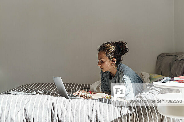 Frau benutzt Laptop  während sie zu Hause auf dem Bett liegt
