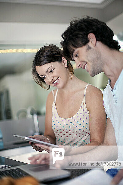 Lächelnde junge Frau  die sich mit ihrem Freund zu Hause ein digitales Tablet teilt