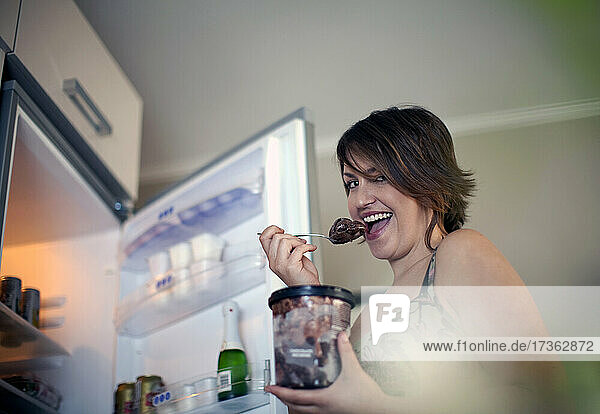 Happy young woman eating ice cream at home