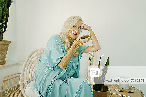 Smiling senior woman sending voicemail through mobile phone at home