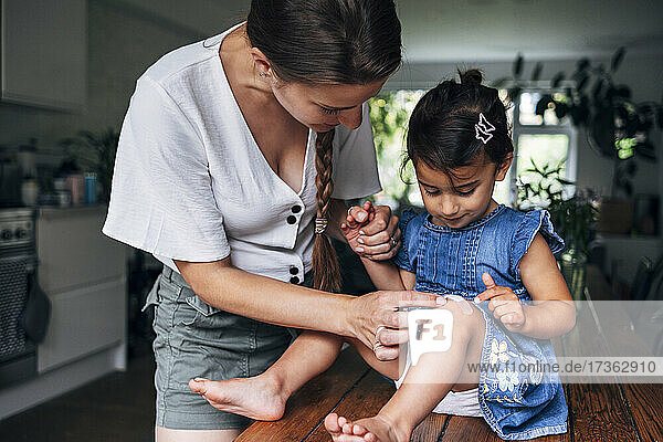 Mutter hält Hand  während sie zu Hause einen Verband auf das Knie ihrer Tochter legt