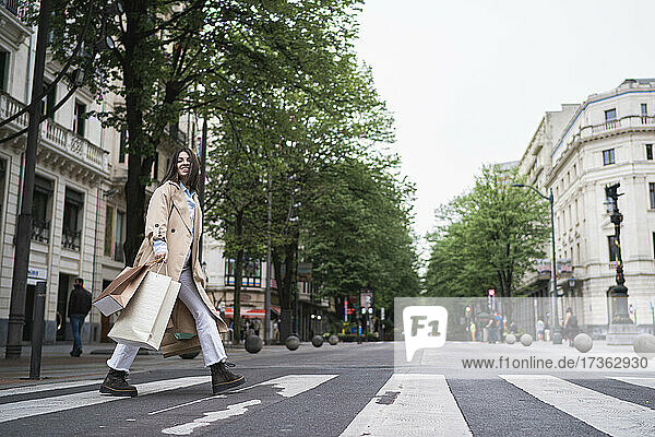 Junge Frau mit Einkaufstüten beim Überqueren der Straße in der Stadt