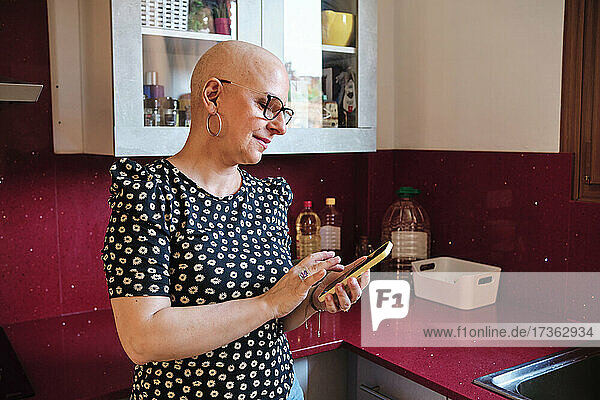 Krebskranke Frau benutzt Mobiltelefon in der Küche zu Hause