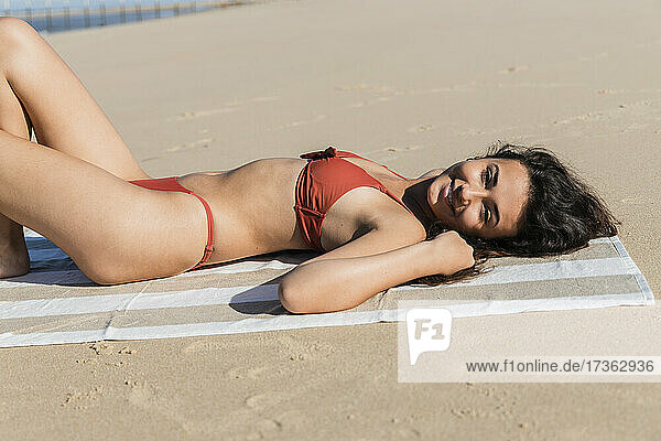 Lächelnde Frau im Bikini auf Sand am Strand liegend