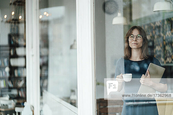 Geschäftsfrau mit Kaffeetasse und Laptop in einem Café  gesehen durch ein Glasfenster