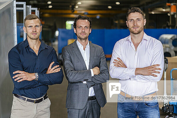 Confident male professionals standing with arms crossed in factory