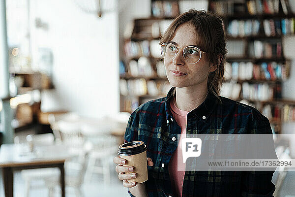 Woman looking away while holding disposable cup in cafe