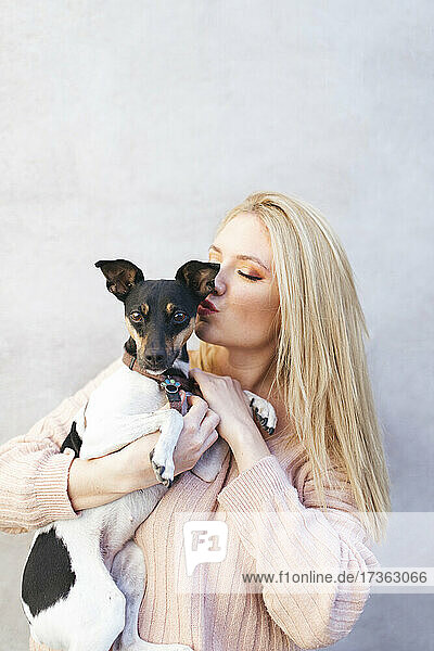 Junge blonde Frau küsst Hund vor der Wand